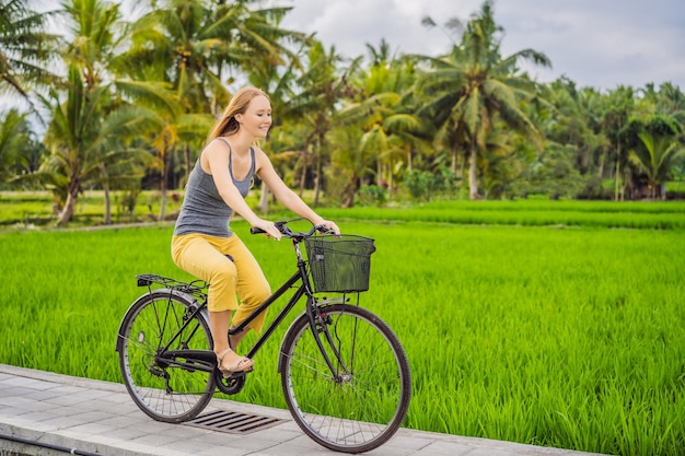 Una giovane donna va in bicicletta su un campo di riso nel concetto di viaggio di ubud bali bali
