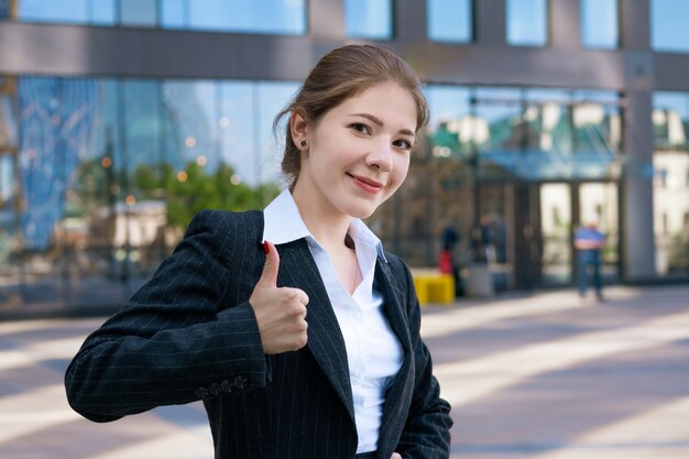 Una giovane donna, vestita con un abito classico e una camicia bianca, si alza con sicurezza e sorride all'aperto.