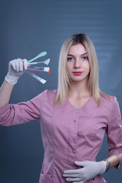 Una giovane dottoressa tiene in mano spazzole cosmetiche per procedure cutanee su sfondo grigio