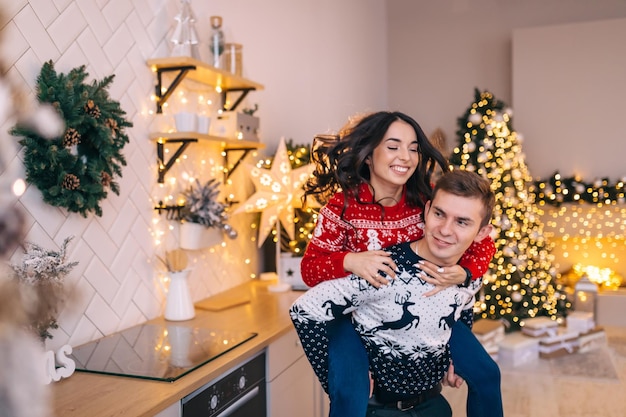 Una giovane e attraente coppia sposata sullo sfondo degli interni di Capodanno e un albero di Natale decorato si divertono