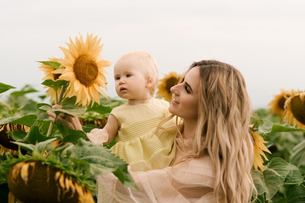 Una giovane e bella madre con la figlia carina in un campo di girasoli