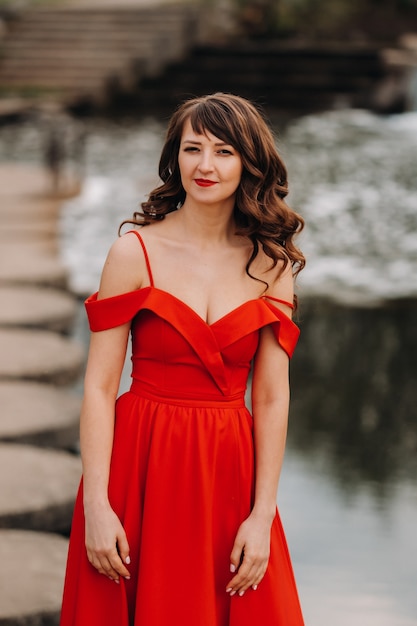 Una giovane e bella ragazza con lunghi capelli castani, in un lungo abito rosso con un anello intorno al lago.