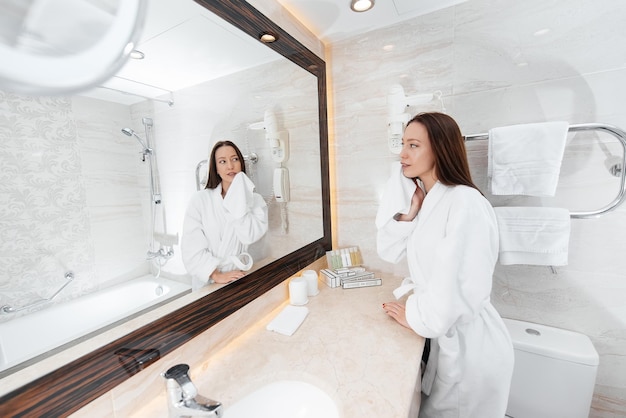 Una giovane e bella ragazza si lava il viso e tiene un asciugamano in un bellissimo bagno bianco Un fresco buongiorno in hotel Riposo e viaggi Ricreazione e turismo in hotel