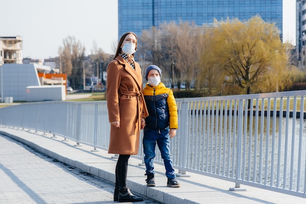 Una giovane famiglia cammina e respira aria fresca in una giornata di sole durante una quarantena e una pandemia. Maschere sui volti delle persone