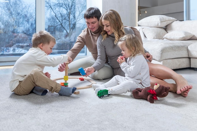 Una giovane famiglia con bambini piccoli gioca in un soggiorno con un divano grigio e grandi finestre Ama la tenerezza e le relazioni in una famiglia amichevole