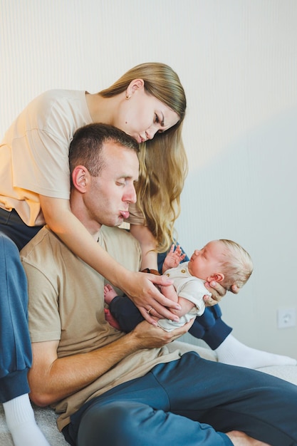 Una giovane famiglia con un neonato una madre e un padre felici che baciano il loro bambino genitori e un bambino sorridente tra le braccia