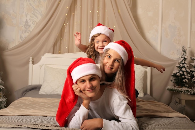 una giovane famiglia con una figlia piccola con i cappelli di Babbo Natale è sdraiata sul letto a casa Natale