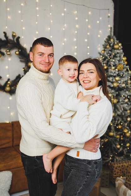 Una giovane famiglia felice con un bambino piccolo festeggia il Capodanno a casa vicino all'albero di Natale Natale in famiglia È tempo di festeggiare il Capodanno