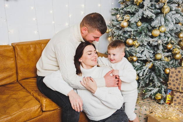 Una giovane famiglia felice con un bambino piccolo festeggia il Capodanno a casa vicino all'albero di Natale Natale in famiglia È tempo di festeggiare il Capodanno