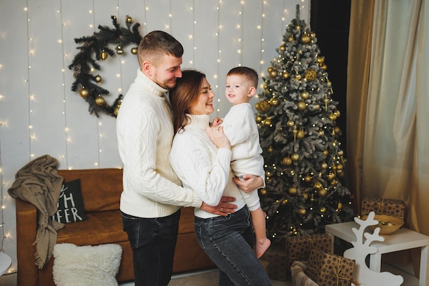 Una giovane famiglia felice con un bambino piccolo festeggia il Capodanno a casa vicino all'albero di Natale Natale in famiglia È tempo di festeggiare il Capodanno