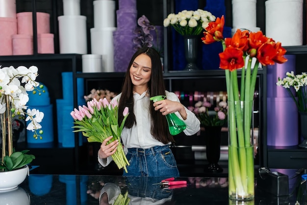 Una giovane fiorista si prende cura dei fiori in un accogliente negozio di fiori e colleziona mazzi di fiori Fioraio e realizzazione di secchi in un negozio di fiori Piccola impresa