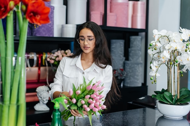 Una giovane fiorista si prende cura dei fiori in un accogliente negozio di fiori e colleziona mazzi di fiori Fioraio e realizzazione di secchi in un negozio di fiori Piccola impresa