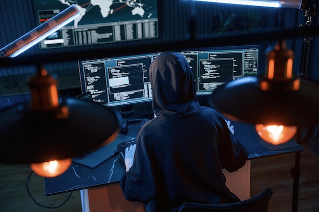 Una giovane hacker professionista è al chiuso davanti a un computer con un sacco di informazioni sugli schermi.