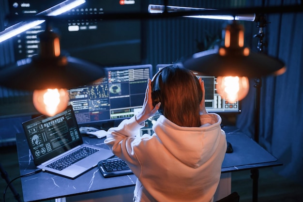 Una giovane hacker professionista è al chiuso davanti a un computer con un sacco di informazioni sugli schermi.