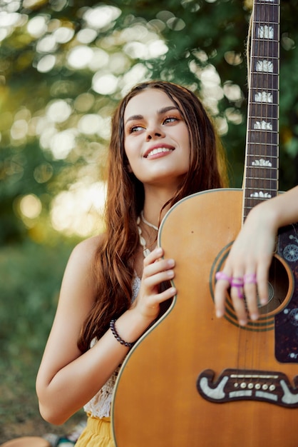 Una giovane hippie con una chitarra in mano sorride dolcemente alla telecamera in un viaggio nella natura stile di vita in armonia foto di alta qualità