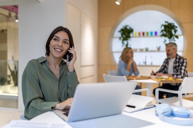 Una giovane impiegata della compagnia sorridente e soddisfatta seduta davanti al computer portatile mentre chiama al cellulare