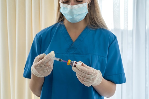 Una giovane infermiera esperta con i capelli biondi in una maschera e guanti sta componendo un vaccino per un paziente. Concetto di medicina. Concetto di vaccinazione