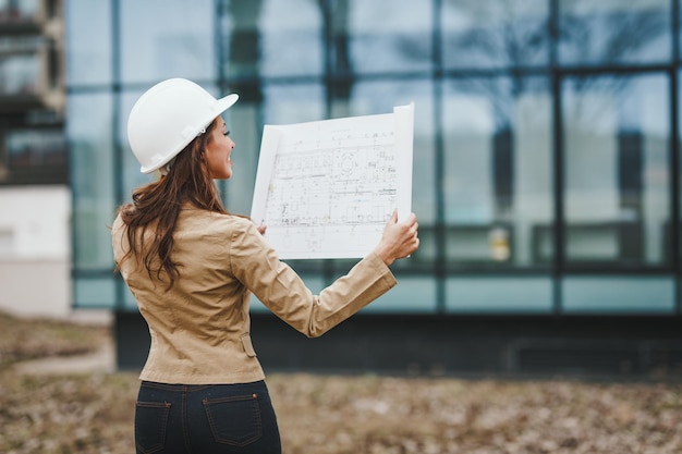 Una giovane ingegnere di successo con casco bianco ha controllato il nuovo progetto e analizzato i progetti davanti al cantiere.