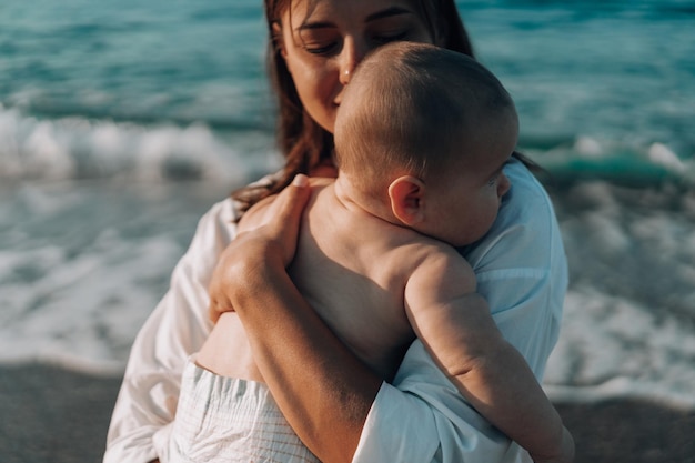 Una giovane madre cammina lungo la spiaggia con un bambino piccolo in pannolini