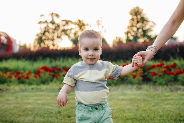 Una giovane madre carina aiuta e insegna al suo piccolo figlio a muovere i primi passi durante il tramonto nel parco sull'erba.