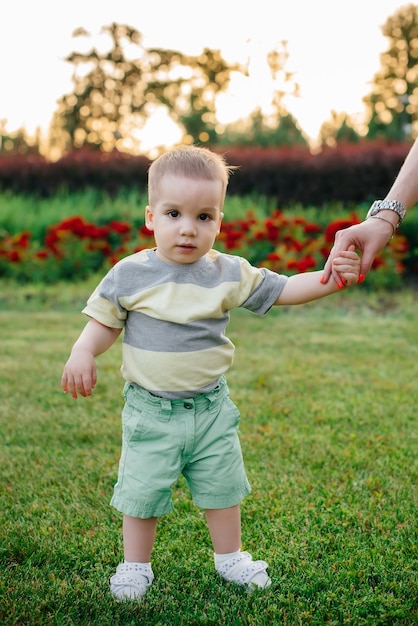 Una giovane madre carina aiuta e insegna al suo piccolo figlio a muovere i primi passi durante il tramonto nel parco sull'erba.