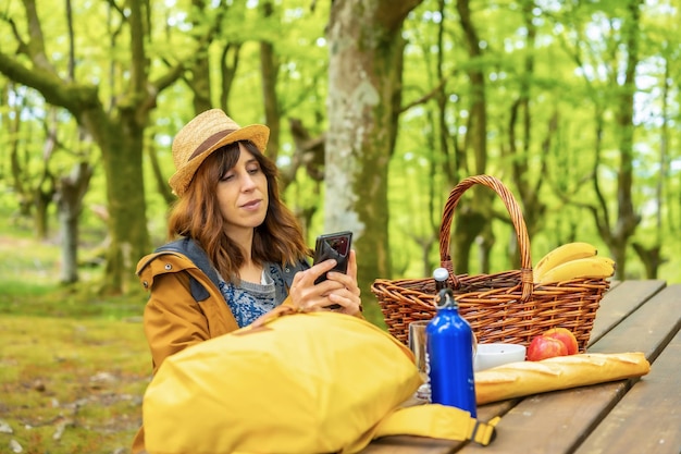 Una giovane madre caucasica guardando il suo cellulare seduto a un tavolo da picnic nei boschi Stile di vita estivo