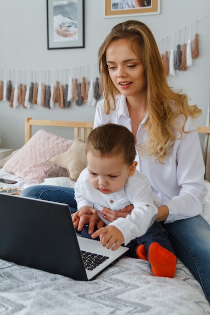 Una giovane madre con il suo amato figlio in camera da letto sul letto con un laptop