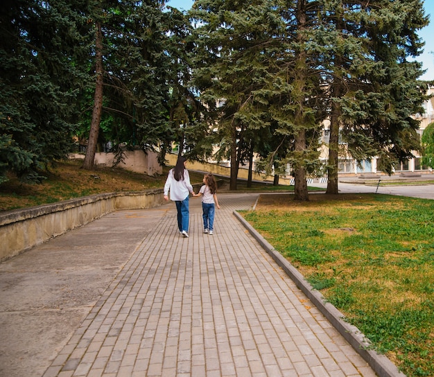 una giovane madre con la sua piccola figlia sta camminando sul marciapiede nel parco.