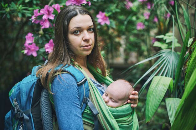 Una giovane madre con un bambino in una fionda sta camminando nella giungla