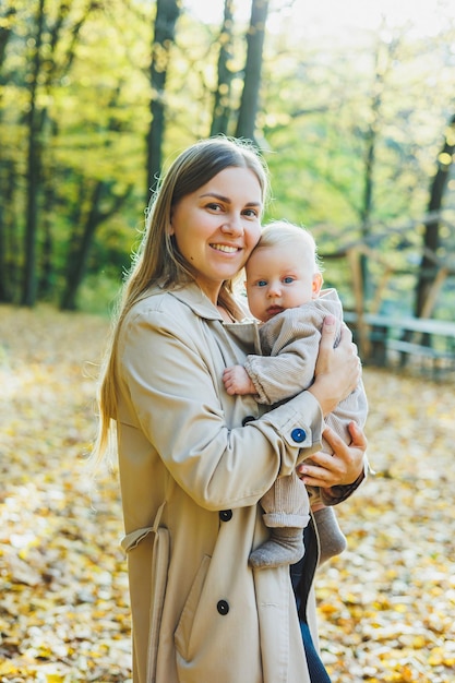 Una giovane madre felice abbraccia il suo piccolo figlio al sole in una calda giornata primaverile o estiva nel parco Il sole splende in un frutteto di mele o in un parco Il concetto di famiglia madre e figlio in natura