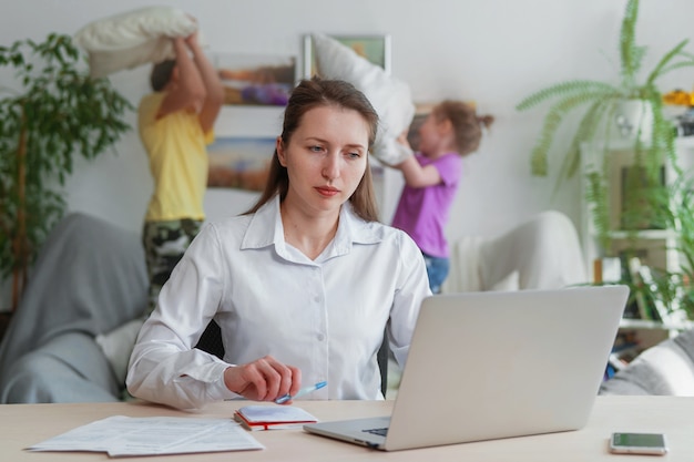 Una giovane madre lavora a casa con un laptop, i bambini interferiscono con il lavoro a distanza.