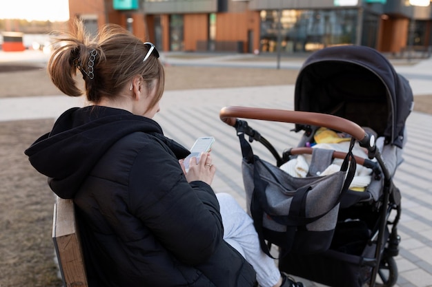 Una giovane madre mentre cammina per strada con il suo bambino si siede su una panchina accanto al passeggino