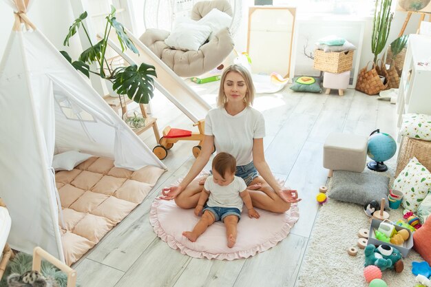 Una giovane madre passa il tempo con la sua bambina a meditare in posizione di loto a casa rilassarsi e superare il concetto di stress