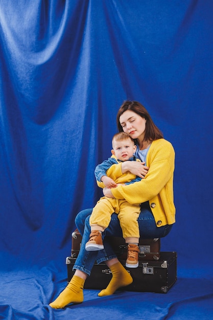 Una giovane madre si siede con un figlio di 3 anni in braccio relazioni familiari con un bambino Istruzione per bambini Mamma con figlio su sfondo blu