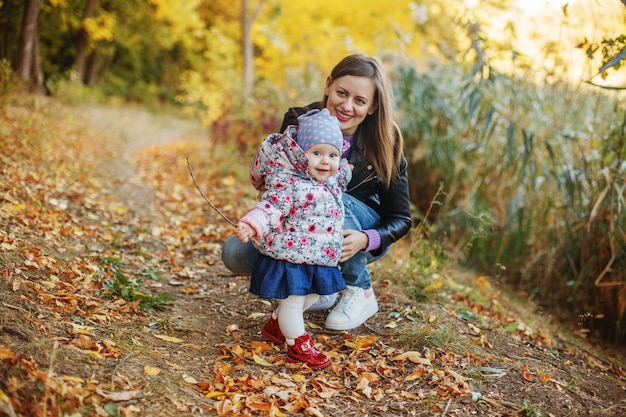 Una giovane madre siede accanto alla sua piccola figlia in un parco in autunno