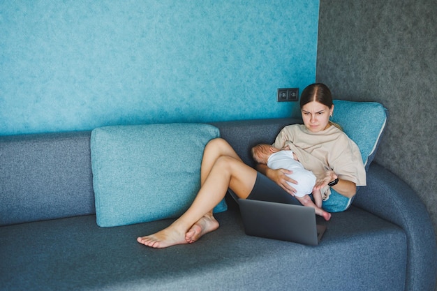 Una giovane madre sorridente sta allattando il suo bambino e sta lavorando a casa con il suo bambino sul divano mentre scrive una e-mail Allattando il bambino Una giovane donna lavora a casa