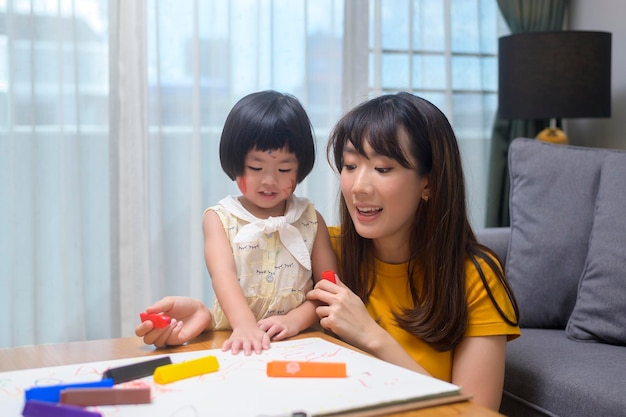 Una giovane mamma che aiuta la figlia a disegnare con matite colorate nel soggiorno di casa.