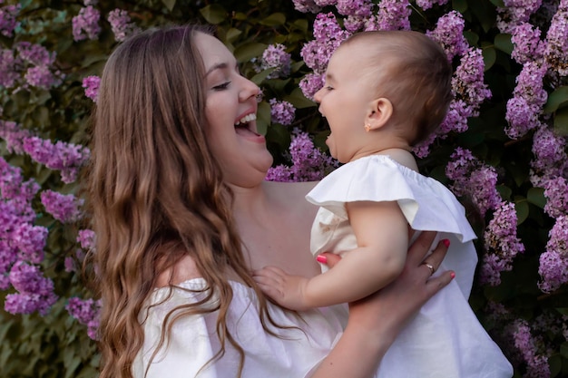 una giovane mamma dai capelli castani in un prendisole bianco abbraccia la sua piccola figlia d contro uno sfondo lilla