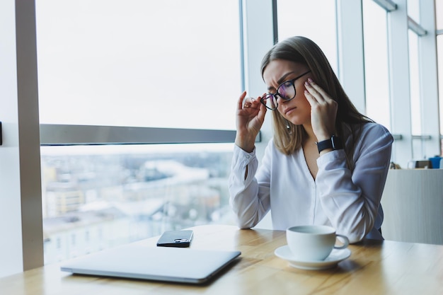 Una giovane manager è stanca dei mal di testa si toglie gli occhiali e si tiene stretta la testa Emicranie dovute a giornate di duro lavoro