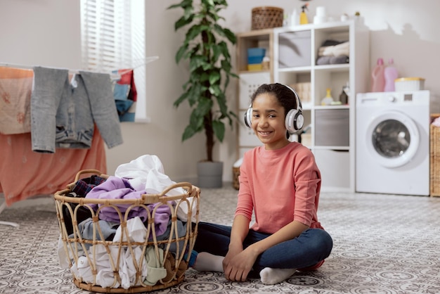 Una giovane ragazza ascolta musica su grandi cuffie wireless mentre fa le faccende domestiche Una ragazza adolescente piega il bucato separa i vestiti