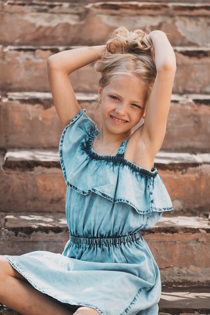 Una giovane ragazza bionda in un vestito blu posa sui gradini delle scale. Foto di alta qualità