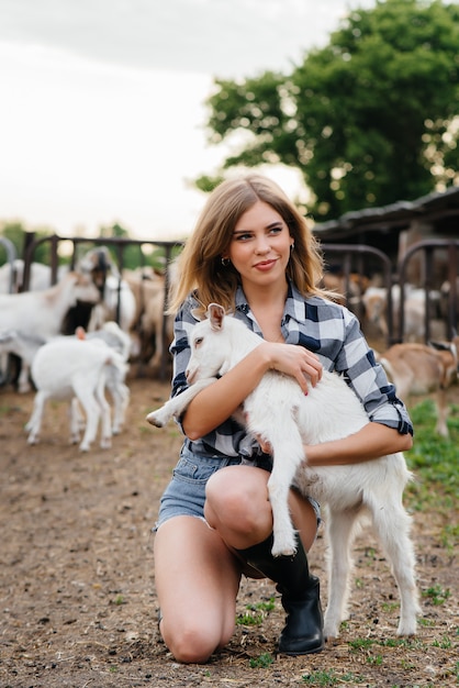 Una giovane ragazza carina posa in un ranch con capre e altri animali. Agricoltura, allevamento di bestiame.