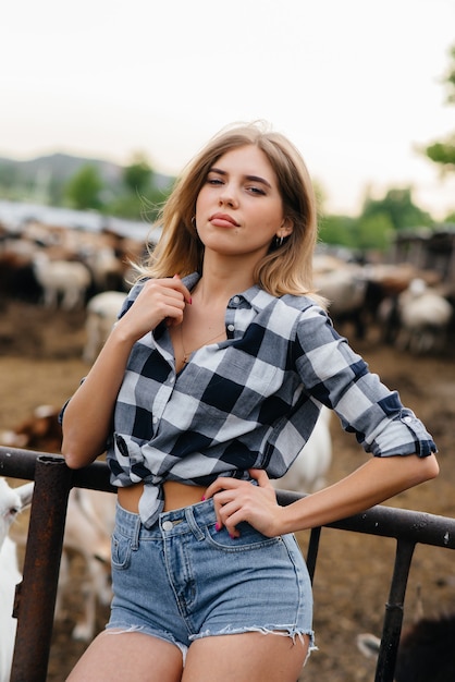 Una giovane ragazza carina posa in un ranch con capre e altri animali. Agricoltura, allevamento di bestiame.