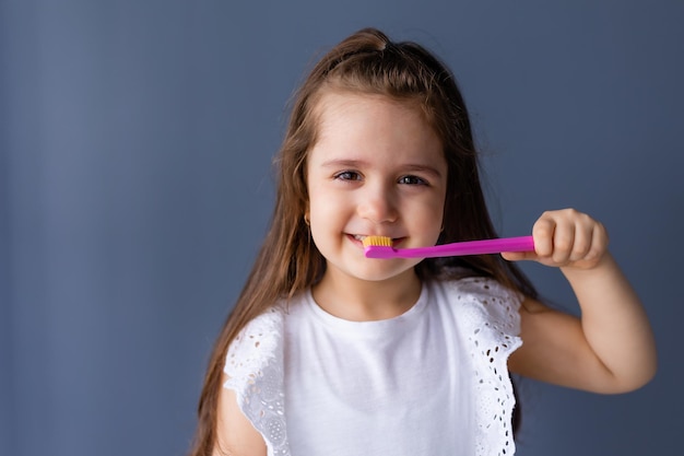 Una giovane ragazza che si lava i denti con uno spazzolino rosa.