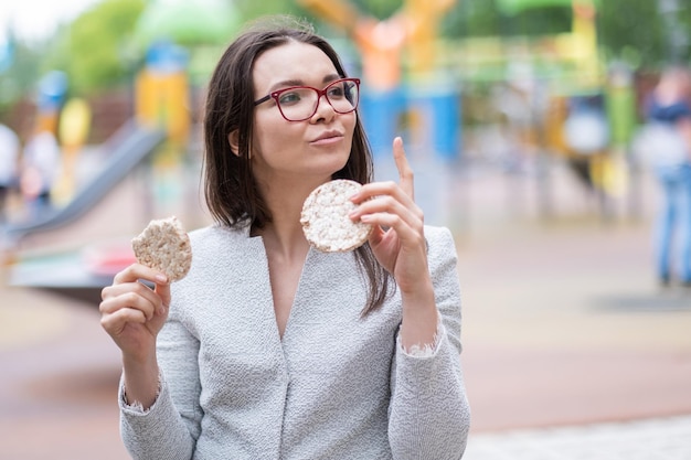 Una giovane ragazza con gli occhiali che mangia pane rotondo per strada