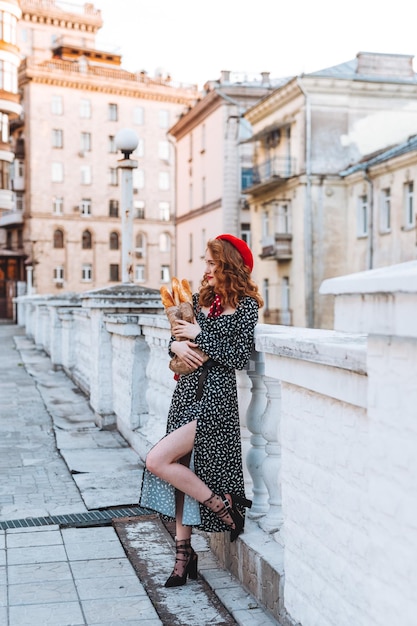 Una giovane ragazza con i capelli rossi in un vestito nero e un berretto rosso sullo sfondo della città