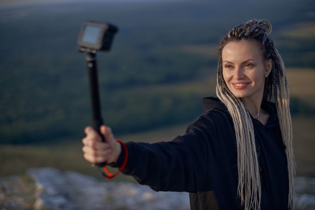 Una giovane ragazza con le trecce registra un vlog sul viaggio in piedi in cima a una montagna il concetto ...