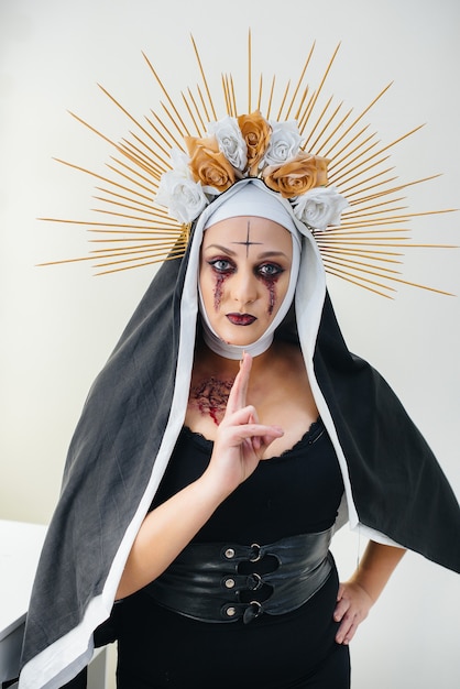 Una giovane ragazza con un bellissimo trucco festivo e un costume da suora spaventoso per le vacanze di Halloween. Felice concetto di Halloween.