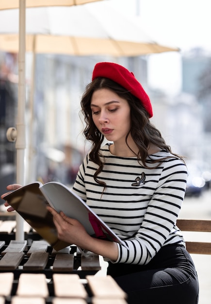 Una giovane ragazza con un berretto rosso e un maglione a righe siede sulla terrazza di un caffè