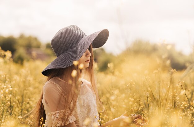 Una giovane ragazza con un cappello cammina su un campo di colza.